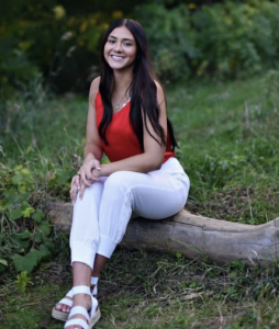 A woman smiles while sitting on a fallen tree trunk.